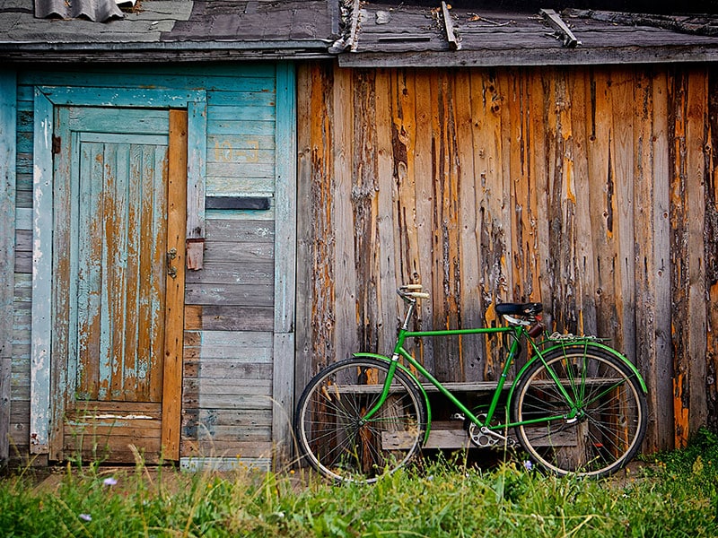 A green bicycle leaning against a dilapidated building.